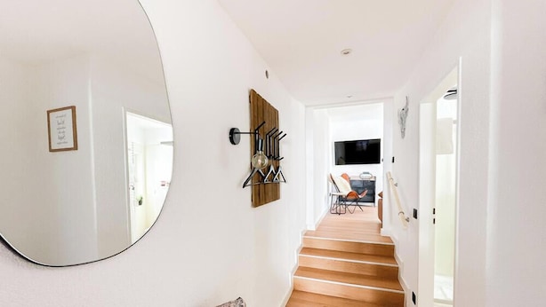 A hallway with a wooden staircase, a round mirror, and a wall-mounted coat rack. - Vacation apartment Alte Liebe & Meer (Cuxhaven)