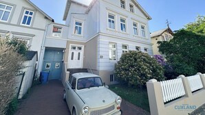 A two-story building with a white facade, a parked vintage car, and a blue door. - Vacation apartment Alte Liebe & Meer (Cuxhaven)