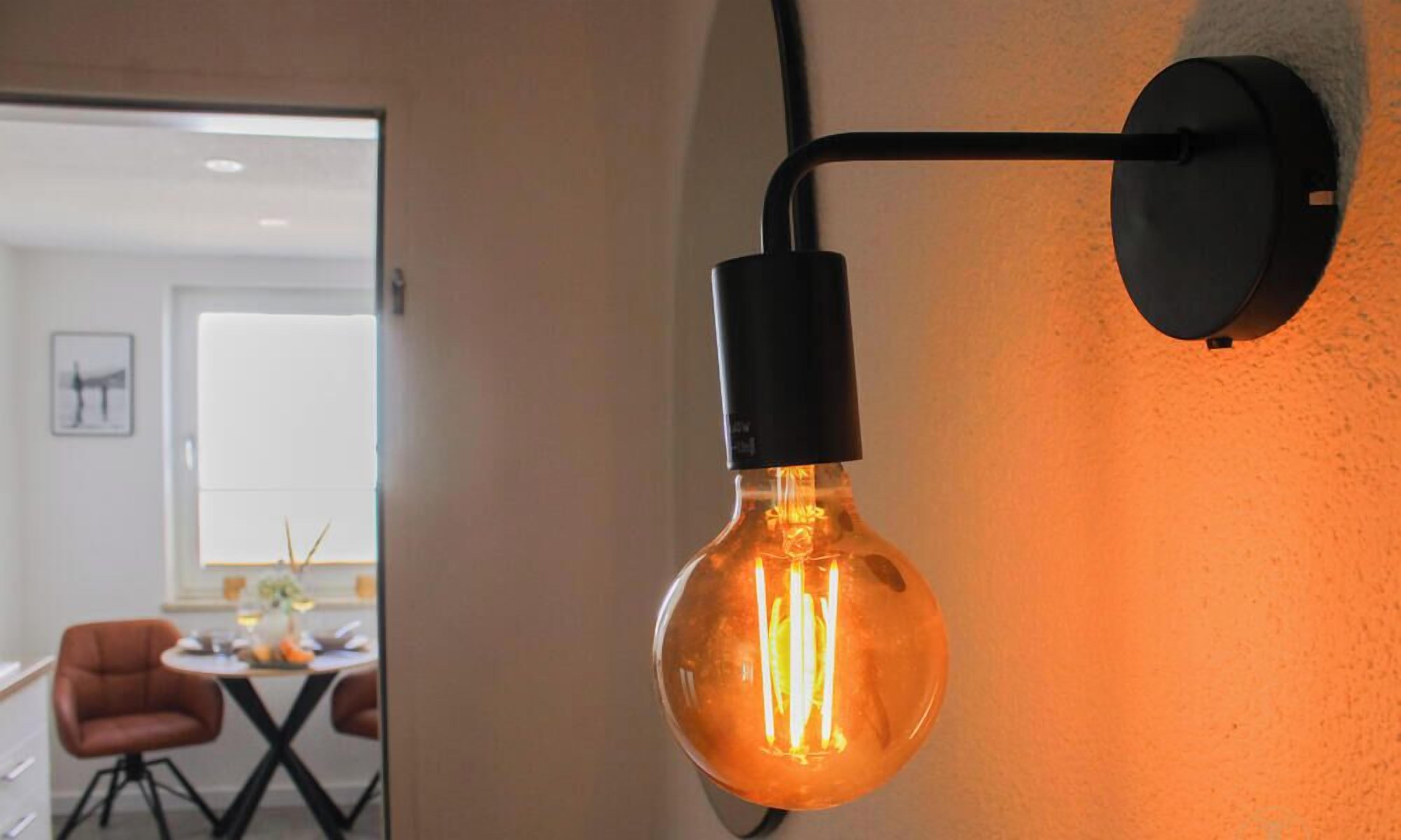 A modern interior with a dining area, a wall-mounted light fixture, and a door leading to another room.