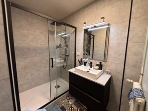 Et moderne badeværelse med en glasafskærmet brusekabine, et toiletbord med spejl og mønstrede fliser.