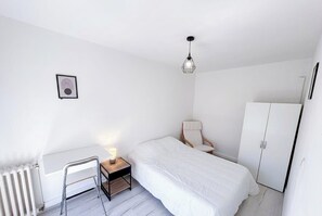 Et minimalistisk soveværelse med seng, stol, skrivebord og garderobeskab.