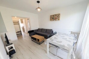 A modern living room with a sectional sofa, a coffee table, a dining table with chairs, a TV, and a radiator. - Bright apartment in the city center with balcony (La Roche-sur-Yon)