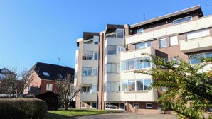 Um edifício residencial de vários andares com telhado plano, janelas amplas e uma escadaria central.