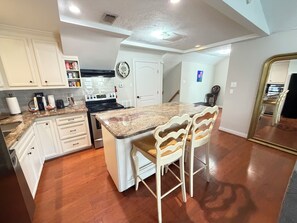 Una cocina con gabinetes blancos, encimera de granito, estufa y dos taburetes de bar.