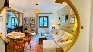 Ein gemütliches Wohnzimmer mit einer Couch, einem Esstisch für vier Personen und einer durch eine offene Tür einsehbarer Küche.