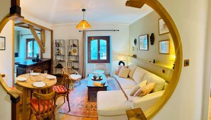 Ein gemütliches Wohnzimmer mit einer Couch, einem Esstisch für vier Personen und einer durch eine offene Tür einsehbarer Küche.