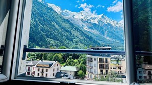 Blick auf Berge durch ein Fenster, mit Gebäuden im Vordergrund.