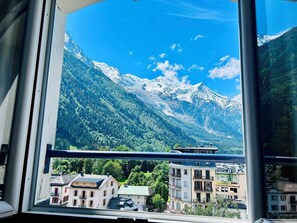 Blick auf Berge durch ein Fenster, mit Gebäuden im Vordergrund.