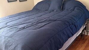 Een bed met een donkerblauwe dekbedovertrek, een wit kussen en een metalen frame.