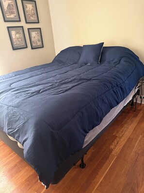 Una cama con edredón azul oscuro, una almohada blanca y estructura metálica.