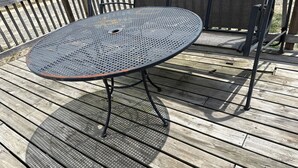 Een ronde metalen tafel met een geperforeerd blad, op metalen poten, staand op een houten terras.