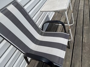 Una silla reclinable a rayas con estructura metálica y una mesita auxiliar a un lado, sobre una terraza de madera.