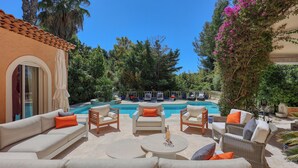 An outdoor seating area with sofas and chairs, a pool, and lush greenery.