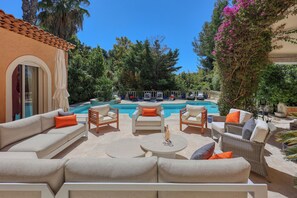 Ein Sitzbereich im Freien mit Sofas und Sesseln, einem Pool und üppiger Bepflanzung.