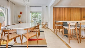 A modern kitchen with a large island, wooden chairs, and a view to the outdoors.