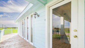 A covered porch with a wooden deck, a white door with a glass panel, and a metal lantern. - The Seashell Suite Cozy 1BR Near the Beach (Bolivar Peninsula)