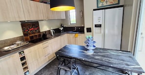 Une cuisine moderne avec des meubles en bois clair, un plan de travail en marbre noir, une bouilloire en acier inoxydable et un réfrigérateur Samsung.