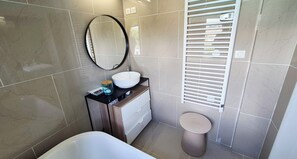 Een badkamer met een bad, een rond spiegel, een wastafel en een toilet.