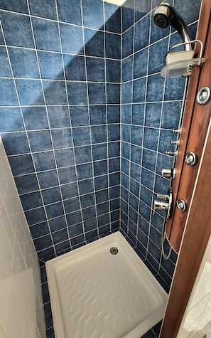 Un petit espace douche carré, avec des carreaux bleus et une baignoire blanche.
