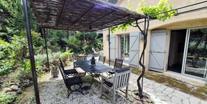 Een terras met een tafel en stoelen, een pergola en een tuin met verschillende planten.