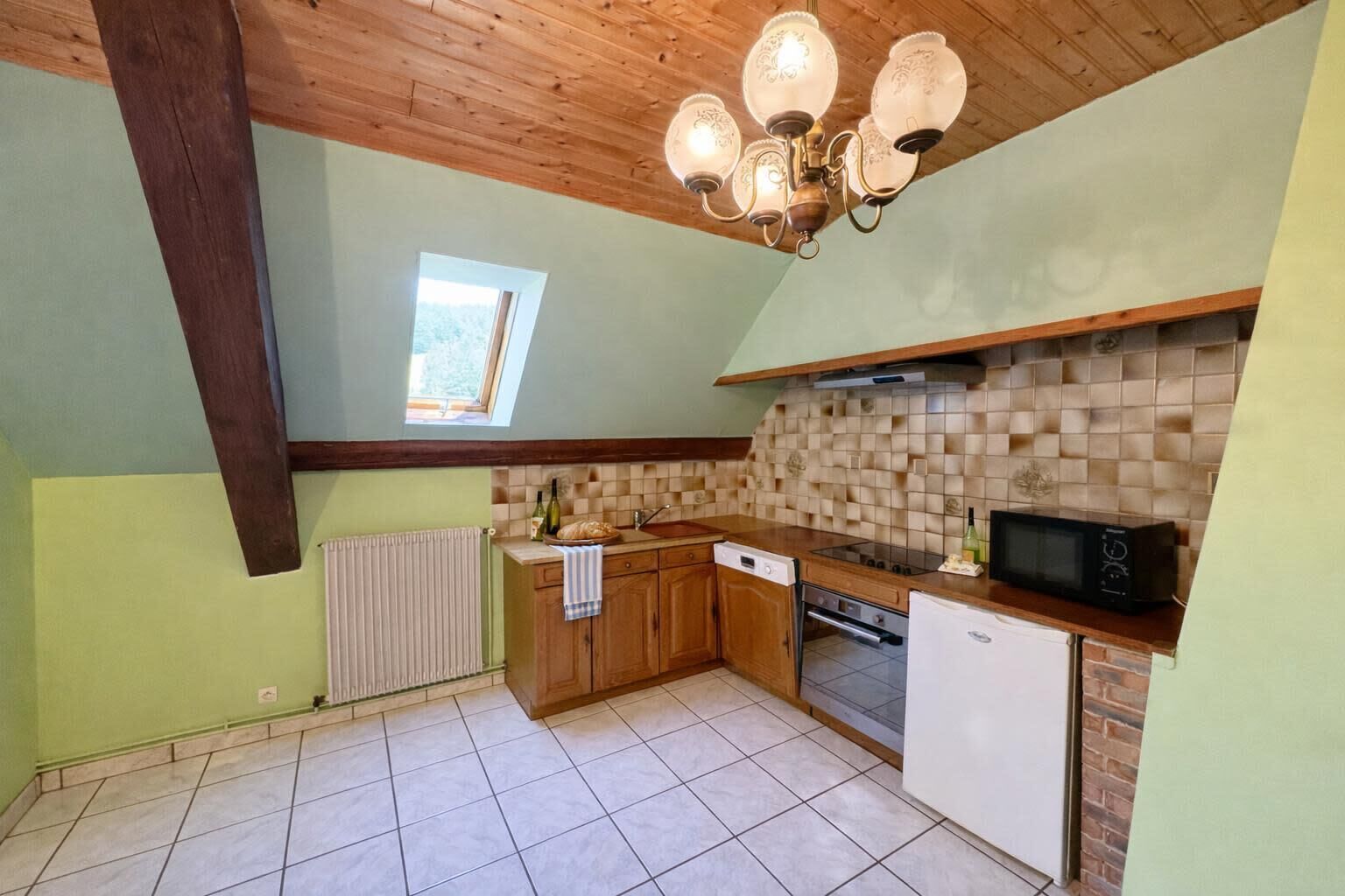 Una cocina con armarios de madera, salpicadero de azulejos, microondas integrado y una ventana.