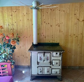 Un poêle ancien orné de motifs floraux, un mur en bois et un pot de fleurs contenant des roses.