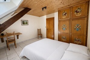 Una camera da letto con un letto, una sedia, una scrivania e un'armadio in legno decorato con motivi floreali.