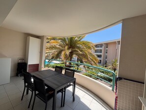 Ein Balkon mit Esstisch und Stühlen, einem Koffer und Blick auf eine Palme und ein Gebäude.