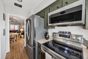 Een moderne keuken met roestvrijstalen apparatuur, een eethoek met rieten meubels en een zichtbaar keukenblok.