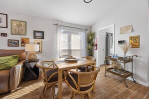 Un salon avec un canapé, une table à manger et des chaises, une lampe et des tableaux encadrés accrochés aux murs.