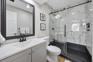 Une salle de bain avec un lavabo blanc, des toilettes, une douche en verre et un grand miroir.
