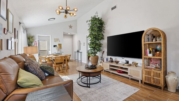 A living room with a brown leather sofa, a round coffee table, a flat-screen TV, a bookshelf, and a large potted plant. - World Cup • Stay 15 Min to Stadium • Private Yard (Arlington)
