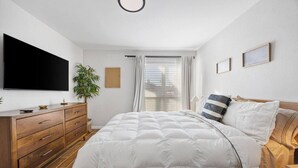 A bedroom with a bed, a TV, a dresser, a plant, and a window with curtains. - World Cup • Stay 15 Min to Stadium • Private Yard (Arlington)
