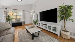Ein modernes Wohnzimmer mit Flachbildfernseher, einer Couch, einem Couchtisch und Topfpflanzen.