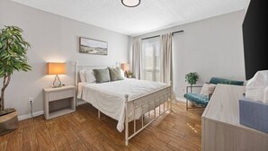 Ein Schlafzimmer mit einem Bett, Nachttischen, einer Lampe, einer Pflanze und einem Fenster mit Vorhängen.