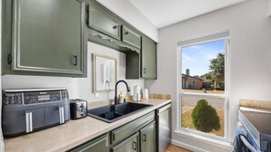 Eine Küche mit eingebautem Toaster, einem Spülbecken und einem Fenster mit Blick auf ein Haus und einen Baum.