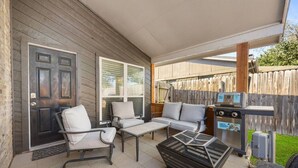 Eine überdachte Terrasse mit Gartenmöbeln, einem Grill und einer Tür.