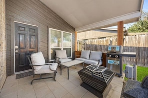 Eine überdachte Terrasse mit Gartenmöbeln, einem Grill und einer Tür.