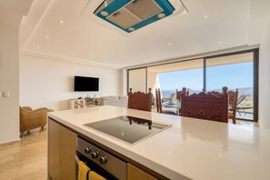 Eine moderne Küche mit einer zentralen Kochinsel, einem an der Wand befestigten Flachbildfernseher und einem großen Fenster mit Blick ins Freie.