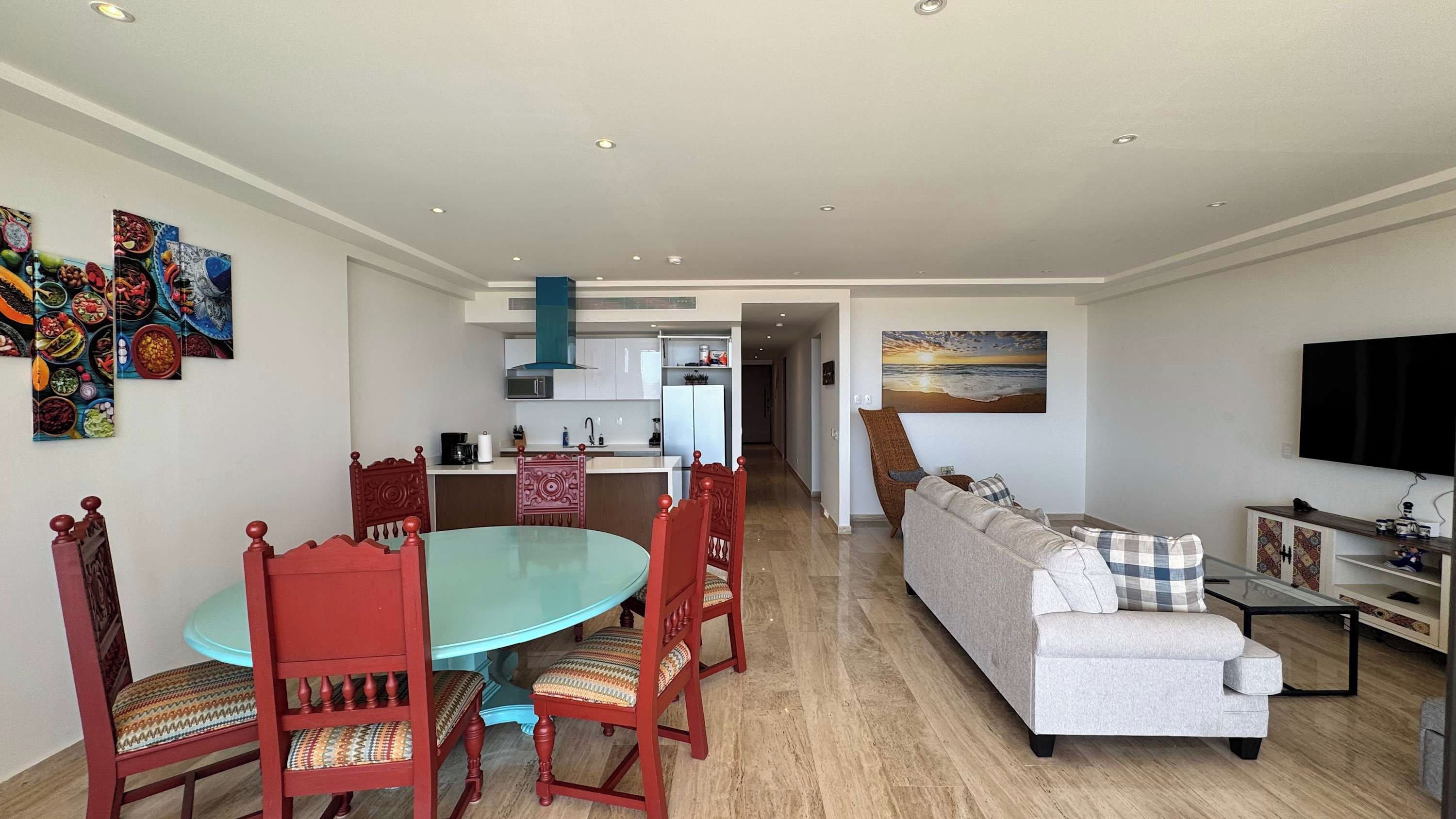 Un salon moderne comprenant un canapé, une table à manger avec des chaises, un coin cuisine et un téléviseur fixé au mur.