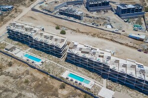 An aerial view of a construction site with multiple buildings under construction, a swimming pool, and a road. - Charming Coastal Resort With Ocean Views, Pool, Gym and Shared Amenities (Cabo San Lucas)