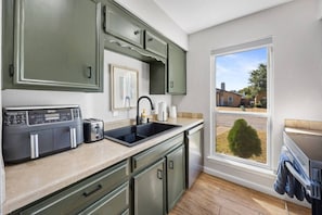 Eine Küche mit eingebautem Toaster, einem Spülbecken und einem Fenster mit Blick auf ein Haus und einen Baum.