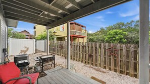A covered outdoor patio with a grill, a red chair, and a wooden fence. - Happy Hound Poolside Retreat (Canyon Lake)