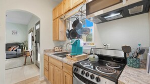 A kitchen with wooden cabinets, a stove, and a coffee maker. - Happy Hound Poolside Retreat (Canyon Lake)