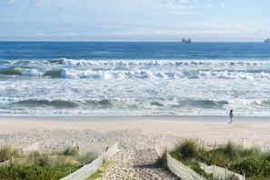 Ein Strand mit einer Person, Wellen und Schiffen in der Ferne.