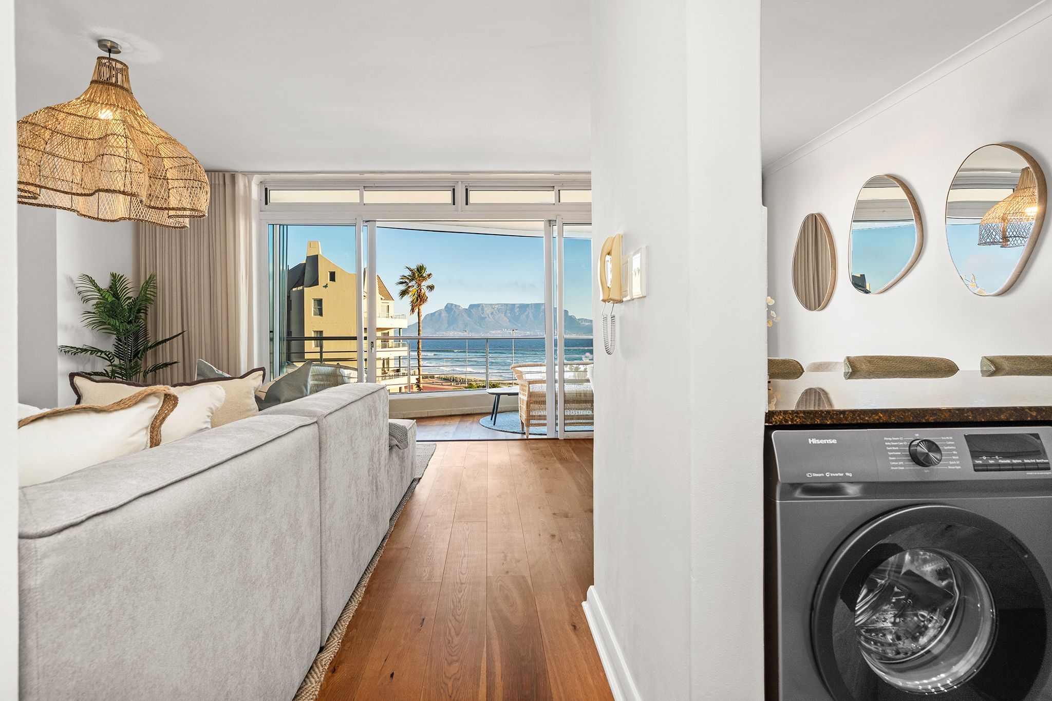 A modern hotel room with a large window, a sofa, a washing machine, and a hanging light fixture.