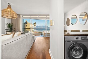 A modern hotel room with a large window, a sofa, a washing machine, and a hanging light fixture. - Portico 306 (Cape Town)