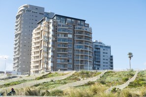 A multi-story residential building with balconies, a landscaped area with pathways, and a clear sky. - Portico 306 (Cape Town)