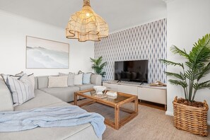 A living room with a sofa, coffee table, TV, and decorative plants. - Portico 306 (Cape Town)