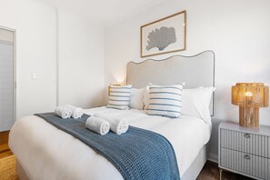 A neatly made bed with rolled towels, a bedside lamp, and a framed artwork on the wall. - Portico 306 (Cape Town)